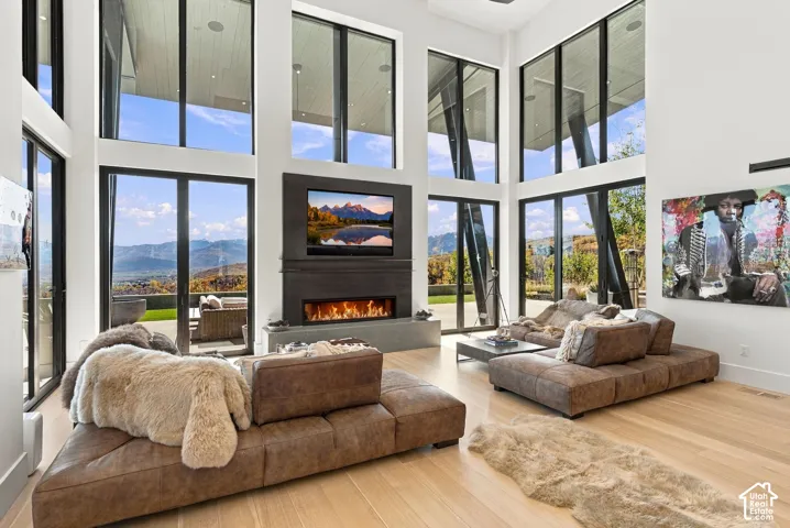 Double-height ceilings with floor-to-ceiling windows, linear fireplace with custom surround, wood-finish flooring, and pass through views toward Park City