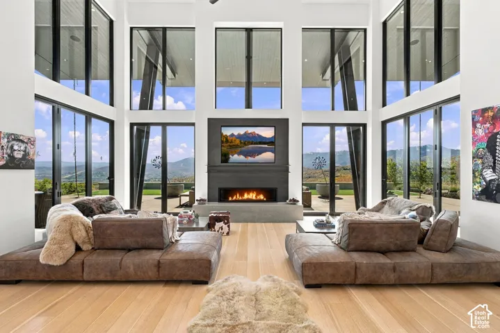 Double-height ceilings with floor-to-ceiling windows, linear fireplace with custom surround, wood-finish flooring, and pass through views toward Park City