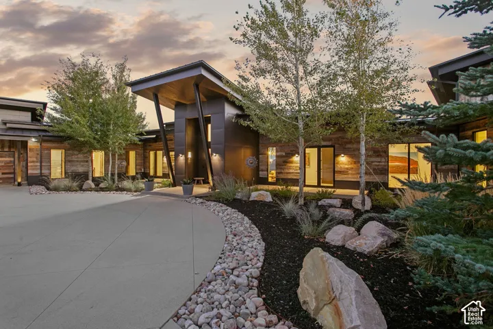 Contemporary exterior featuring wood-plank siding, metal-panel accents, a covered entrance with angled structural supports, concrete motor court, and landscaped rock gardens