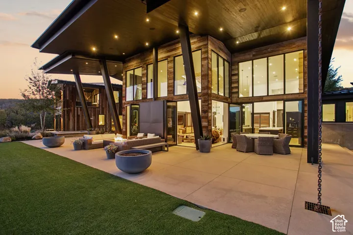 Modern architectural residence with expansive outdoor living spaces featuring a composite patio, mature landscaping with manicured lawn, and integrated outdoor seating areas