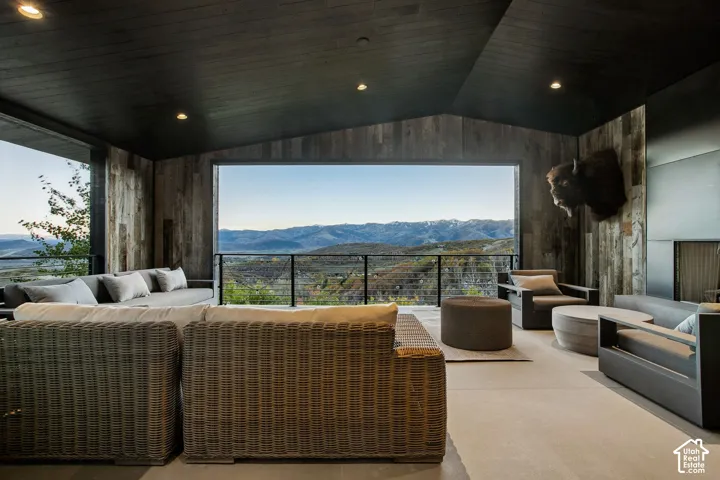 Covered outdoor living space featuring a black wood-paneled ceiling, reclaimed wood wall cladding, recessed lighting, and a metal cable railing overlooking mountain scenery