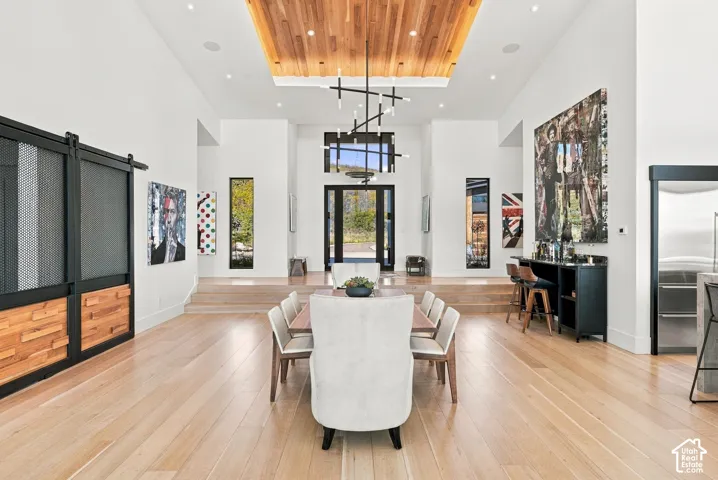 High-ceiling space featuring wood-finish flooring, a wood-paneled tray ceiling, custom black-framed sliding barn doors with wood inlay, and a multi-tiered modern pendant light fixture