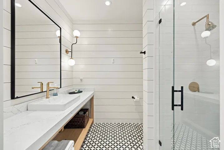 Bathroom featuring horizontal shiplap walls, a custom floating vanity with a stone countertop, a vessel sink with a gold-tone faucet, a glass-enclosed shower with gold-tone fixtures, and patterned tile flooring