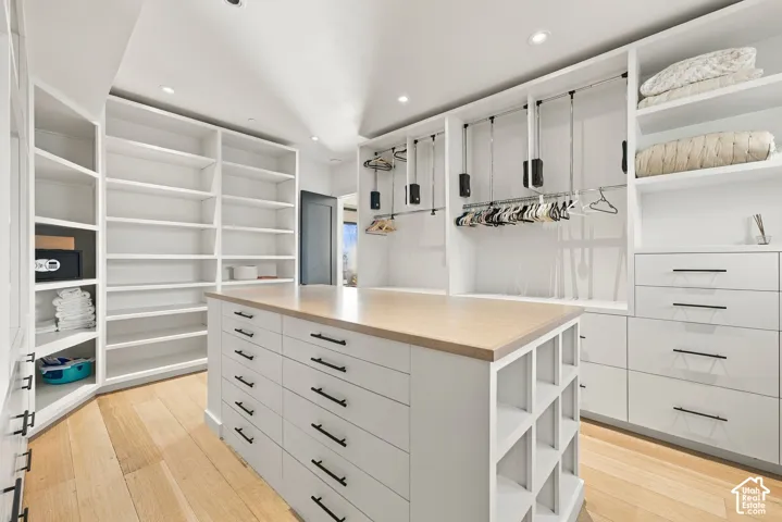 Custom walk-in closet in Primary Suite, featuring floor-to-ceiling built-in shelving, a central island with storage drawers and quartz countertop, wood-finish flooring, and integrated laundry