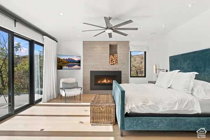 Primary bedroom featuring views toward Park City, wide-plank wood-finish flooring, floor-to-ceiling sliding glass doors, horizontal wood-paneled accent wall, built-in gas fireplace