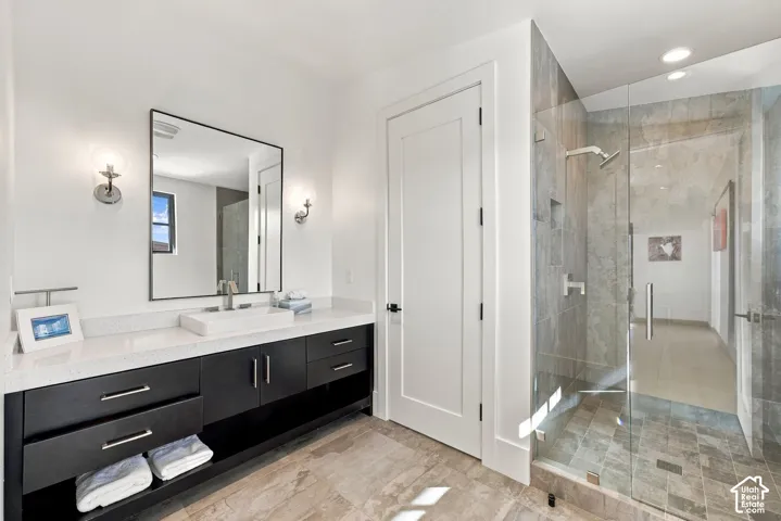 Modern vanity in office bathroom with dark cabinetry, vessel sink, and quartz countertop, paired with a walk-in shower featuring glass enclosure, recessed shelving, and stone-finish tile surround