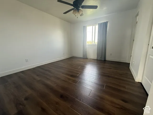 Room featuring wood-finish flooring, neutral walls, single-pane window, and a multi-blade ceiling fan with integrated light fixture