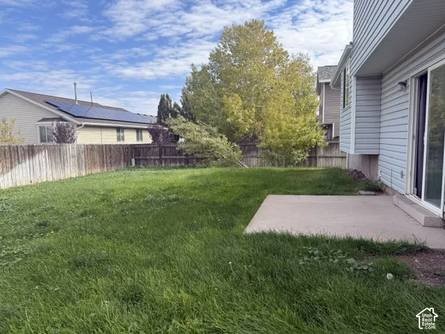 Backyard featuring a concrete patio, grassy lawn, wood privacy fencing, and mature trees