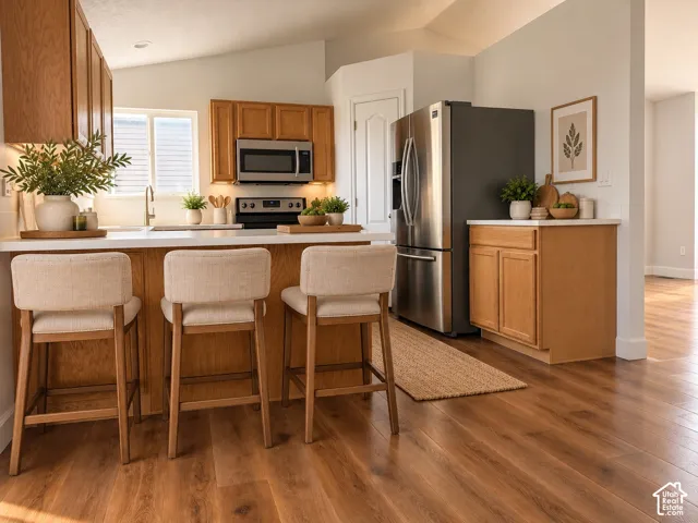 Kitchen featuring wood-finish cabinetry, stainless steel appliances, quartz countertops, and wood-finish flooring under a vaulted ceiling