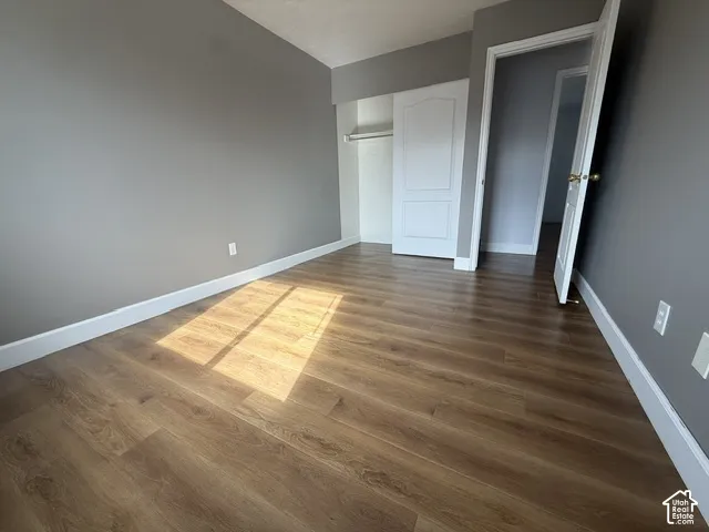 Neutral grey wall paint, wood-finish flooring, and a closet with a built-in shelving rod featuring a white panel door