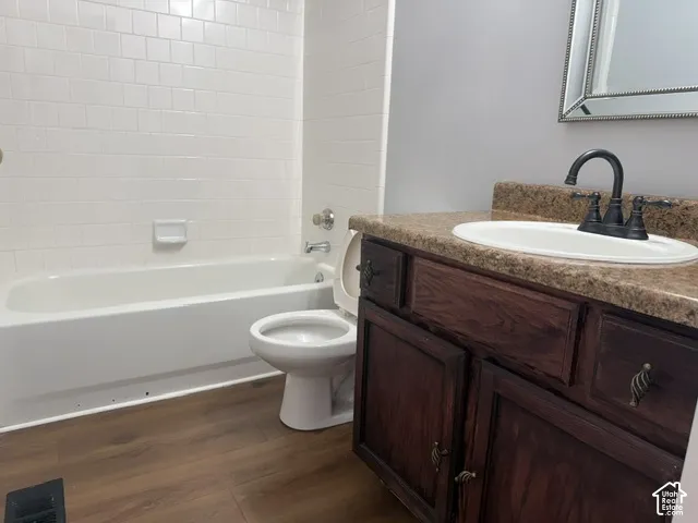 Bathroom featuring wood-finish flooring, dark wood-tone cabinetry, stone-texture countertop with an integrated basin, and white subway-style tile shower surround
