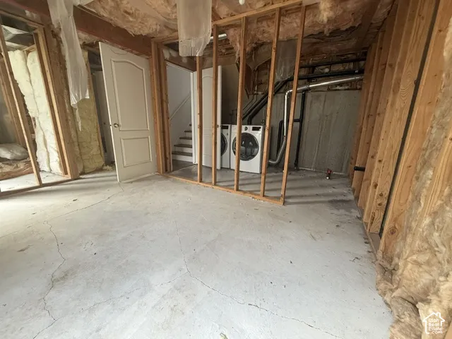 Unfinished interior space featuring exposed wood framing, concrete flooring, and built-in laundry appliances