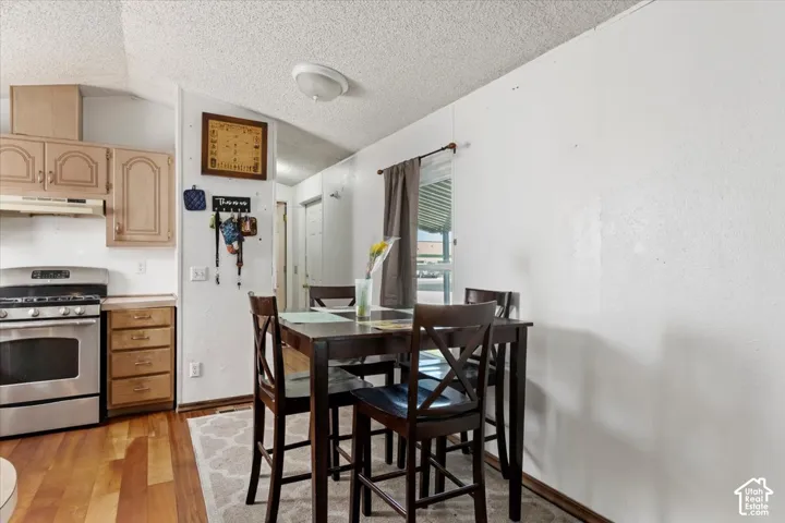 Kitchen featuring wood-finish cabinetry, stainless steel range with integrated vent hood, and wood-finish flooring