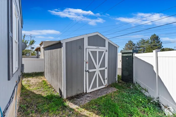 Exterior storage shed featuring a gabled roof and white vinyl privacy fencing