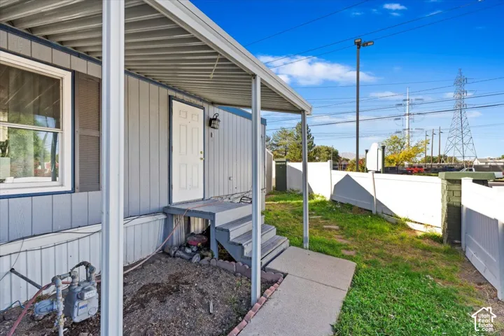 Covered exterior entryway featuring vertical siding, metal roofing, attached stairs, and a white vinyl perimeter fence