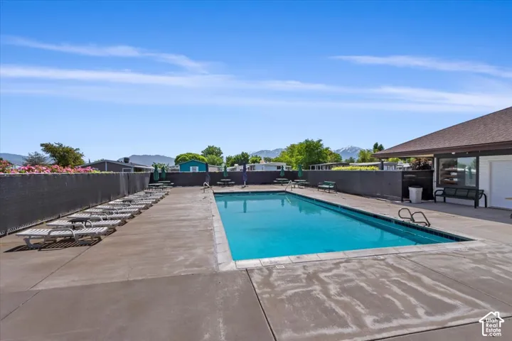 In-ground swimming pool featuring a concrete surround, enclosed by a privacy fence with a mountain backdrop