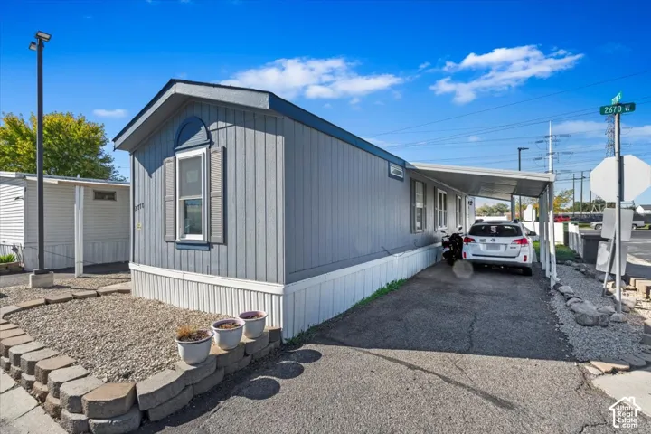 Single-story exterior featuring vertical light grey siding, a front-facing arched window, decorative shutters, and an attached covered carport