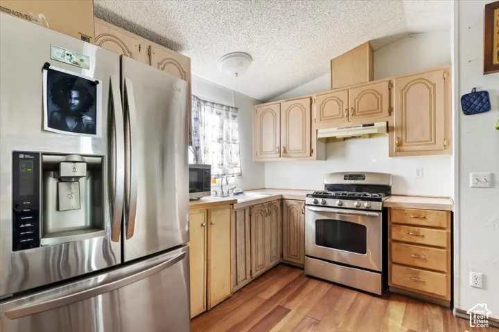Kitchen featuring stainless steel refrigerator, stainless steel gas range, wood cabinetry, and wood-finish flooring