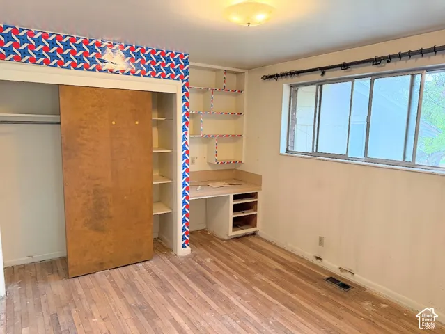 Bedroom featuring wood-finish flooring, a sliding-door closet, a built-in desk with integrated shelving, and a large multi-pane window