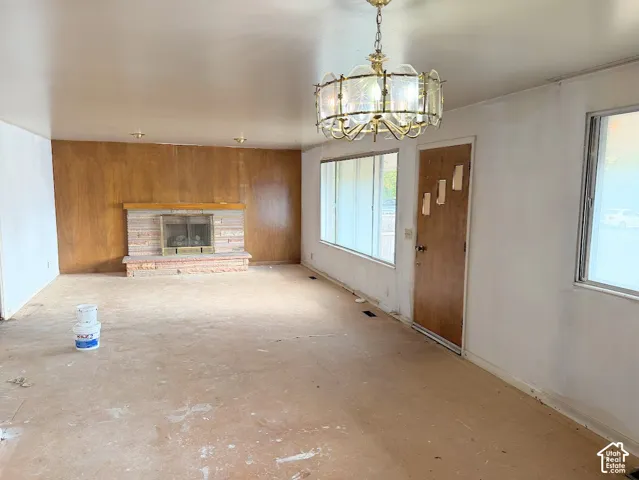 Fireplace featuring a masonry surround and wood mantel, wood-paneled accent wall, ornate multi-arm chandelier, and large windows