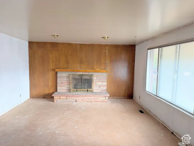 Fireplace with stacked stone hearth and wood mantelpiece, wood-paneled accent wall, and large picture window