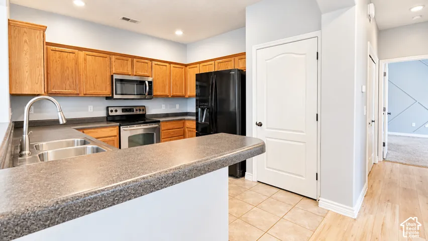 Kitchen featuring wood cabinetry, solid-surface countertops, dual-basin stainless steel sink, stainless steel appliance suite, and tile flooring