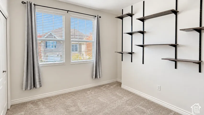 Neutral-toned carpeted flooring, two dual-pane windows, and wall-mounted dark metal shelving units