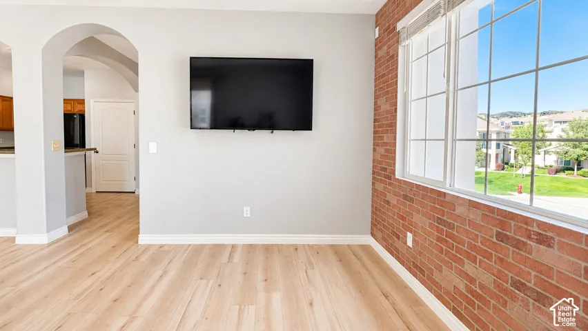 Exposed brick accent wall, wood-finish flooring, and arched architectural detailing, featuring large windows and neutral wall tones