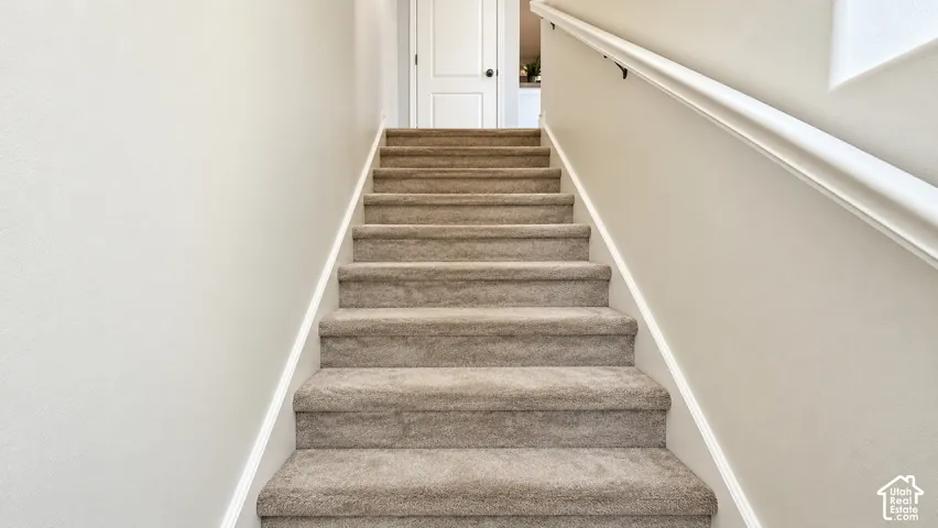Staircase featuring wall-to-wall carpeting, neutral-toned walls, and a white handrail