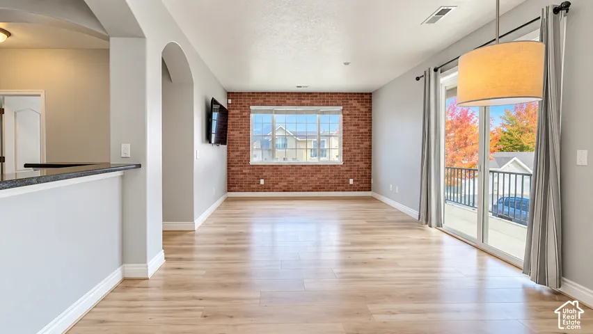 Interior space featuring wood-finish flooring, a decorative brick accent wall, arched architecture, sliding glass patio doors, and a suspended drum pendant light