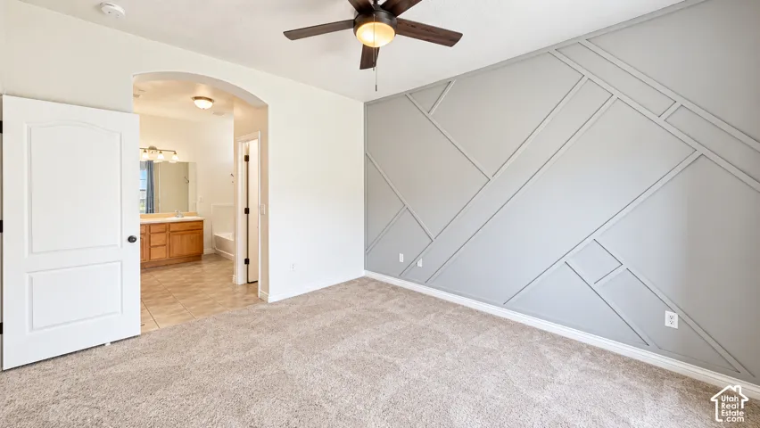 Room featuring a grey geometric wall accent, neutral carpeting, and a ceiling fan with integrated lighting