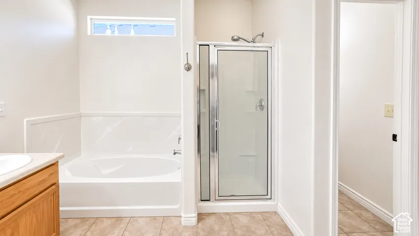 Built-in soaking tub with surround, glass-enclosed shower, light wood-finish vanity, and tile flooring