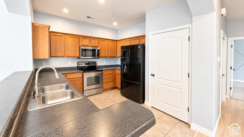 Kitchen featuring oak cabinetry, dark solid-surface countertops, stainless steel appliances, ceramic tile flooring, and a stainless steel dual-basin sink with a high-arc faucet