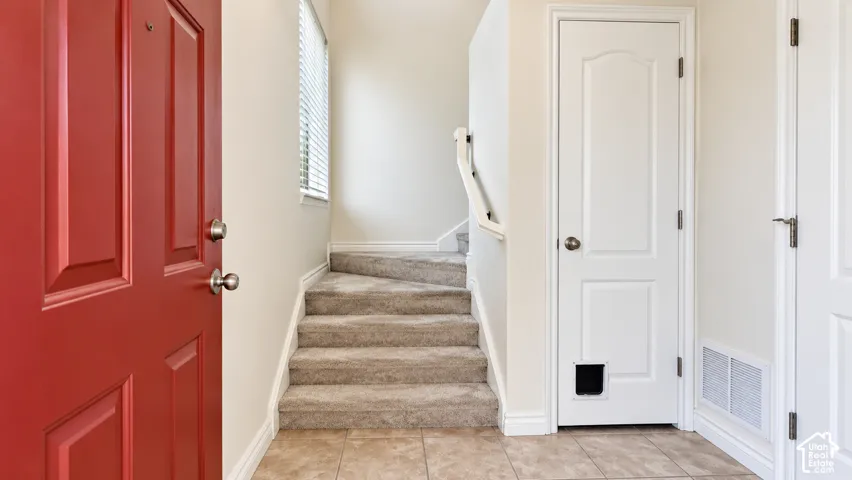 Entryway featuring a bold red door, neutral tile flooring, carpeted stairs, and a white interior door with a built-in pet portal