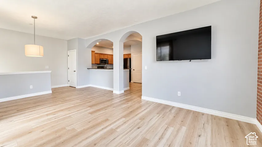 Open interior space featuring light wood-finish flooring, architectural arched openings, and a red brick accent wall