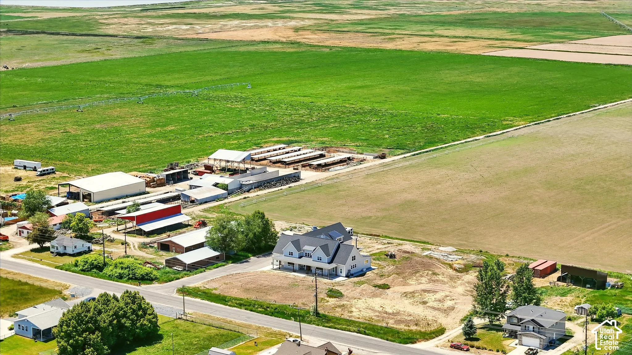 Aerial perspective featuring extensive acreage, multiple agricultural outbuildings, covered livestock pens, and a multi-level residence with a gabled roofline