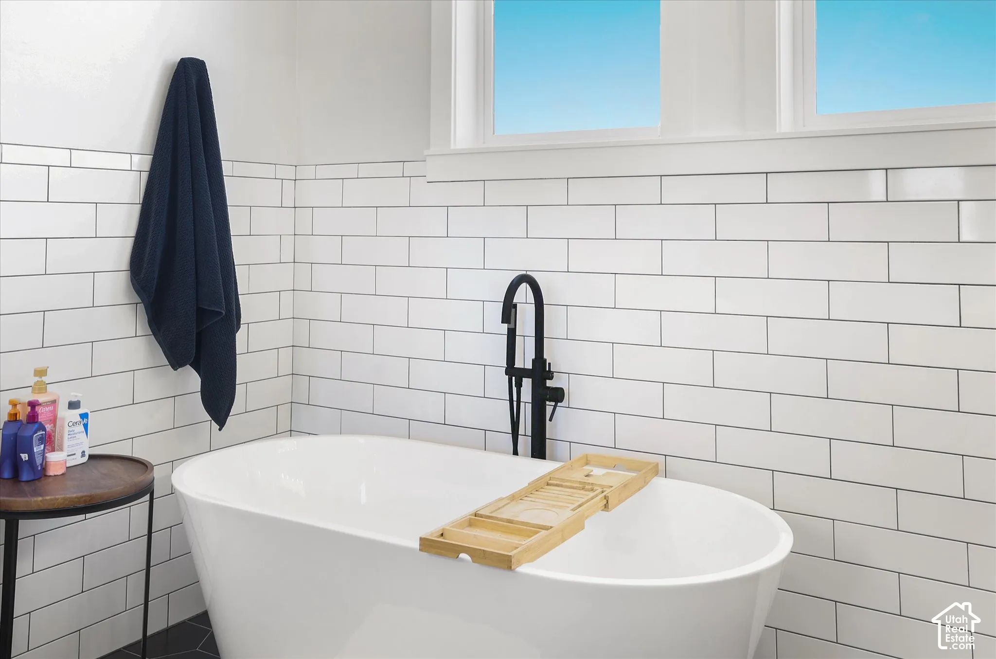 Freestanding soaking tub featuring a matte black floor-mounted faucet and white subway tile wall surround