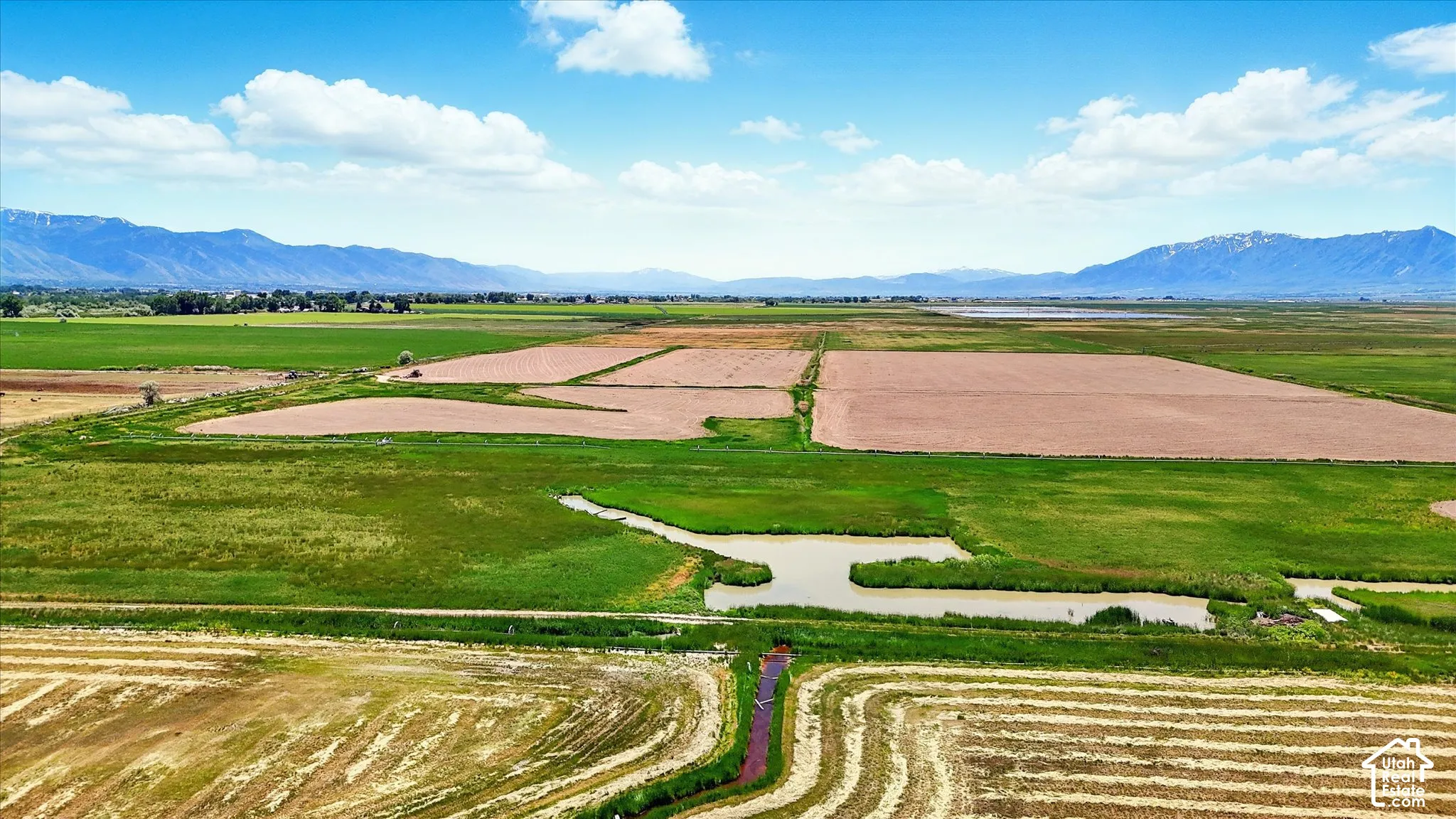 Expansive acreage featuring cultivated fields, a natural pond, drainage channels, and mountain backdrops
