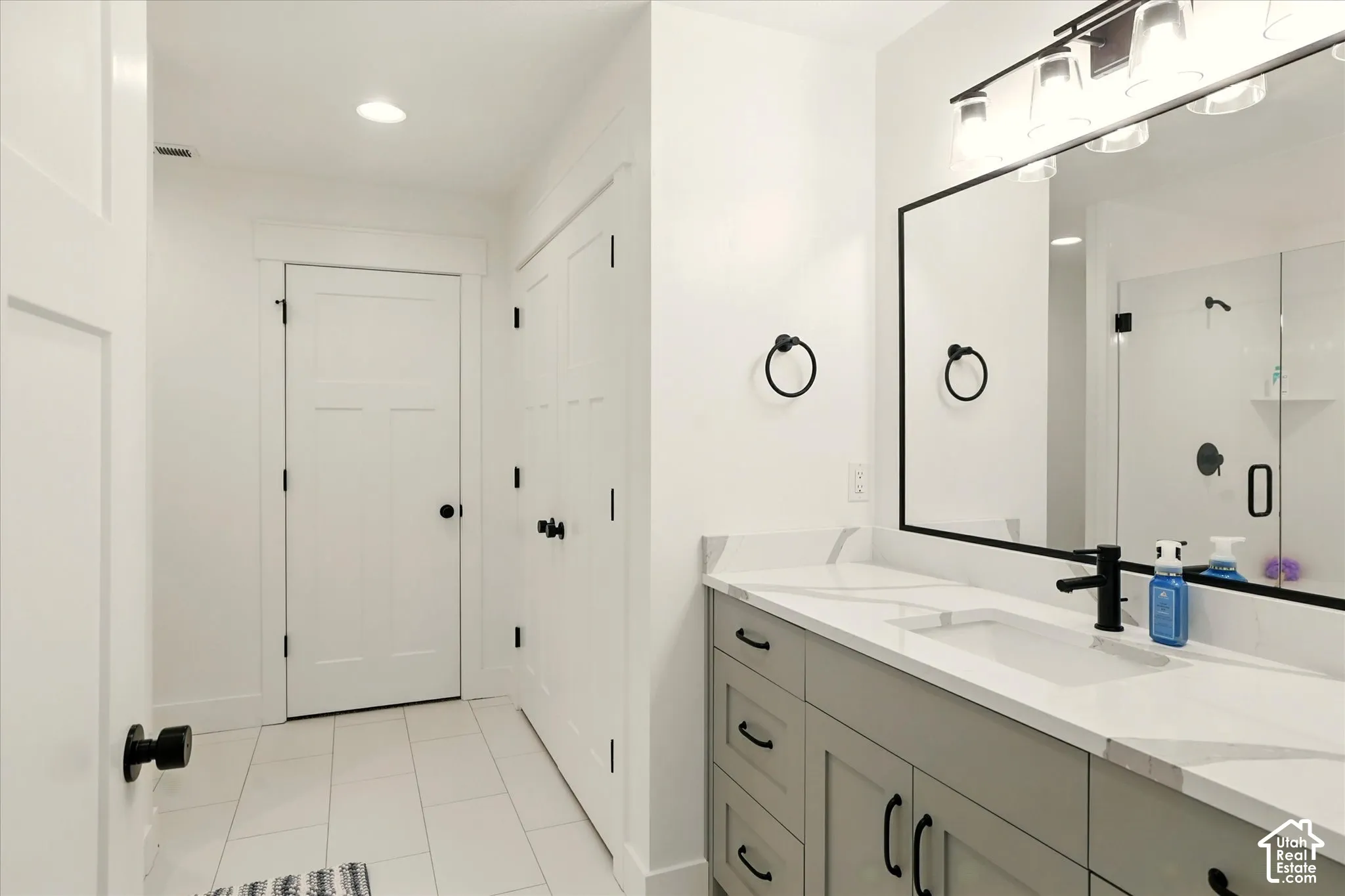 Vanity with stone-finish countertop and integrated sink, matte black hardware, framed vanity mirror, and tile flooring