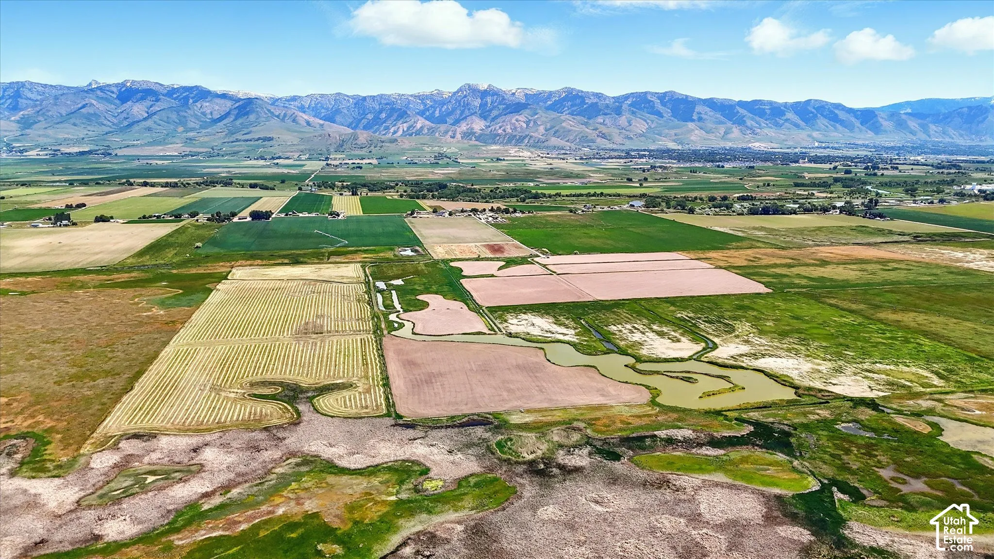Expansive acreage featuring natural water channels, diverse agricultural fields, and prominent mountain range backdrop