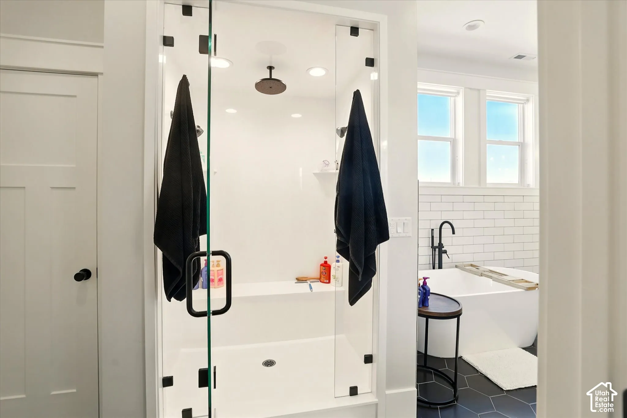 Walk-in shower featuring a glass enclosure with matte black hardware, integrated bench seat, and ceiling-mounted rainfall showerhead, plus two additional shower heads,  paired with a freestanding soaking tub with matte black floor-mounted faucet and subwa