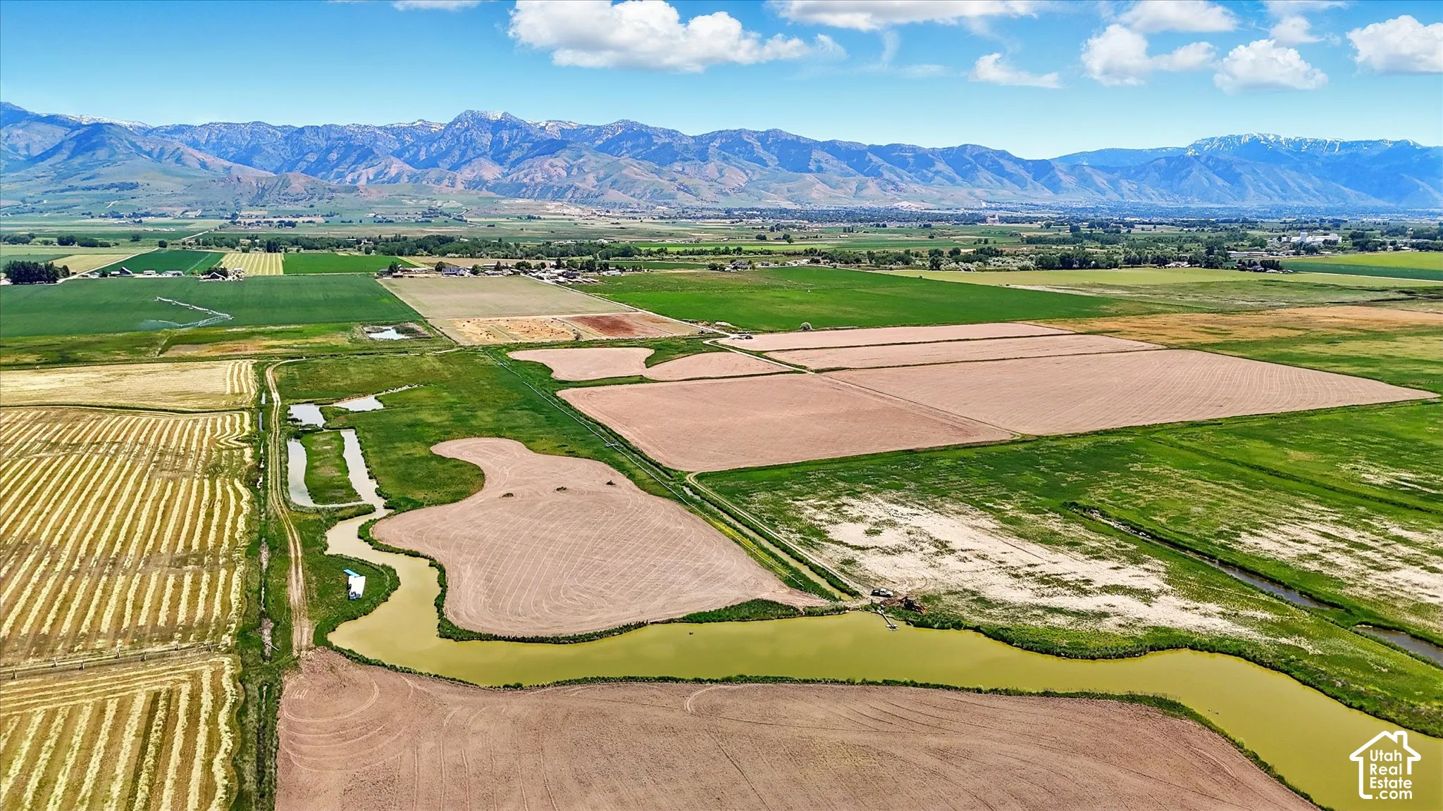 Expansive acreage featuring irrigated farmland, open fields, a natural waterway, and mountain range scenery