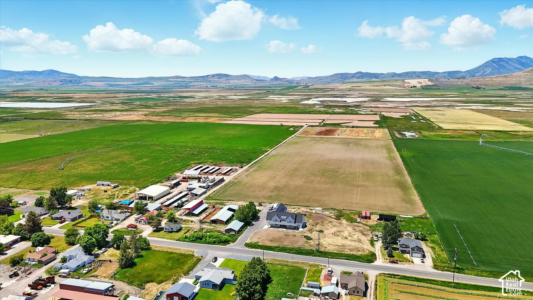 Aerial perspective of expansive agricultural acreage featuring multiple outbuildings, large-scale grazing areas, road access, and prominent mountain backdrops