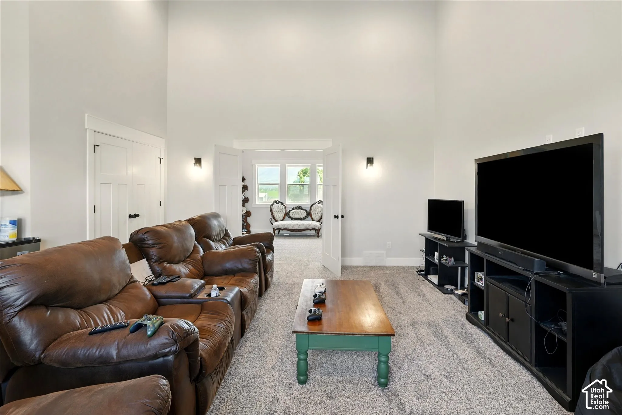 Expansive room featuring vaulted ceilings, neutral wall color, carpeting, and double-door entry