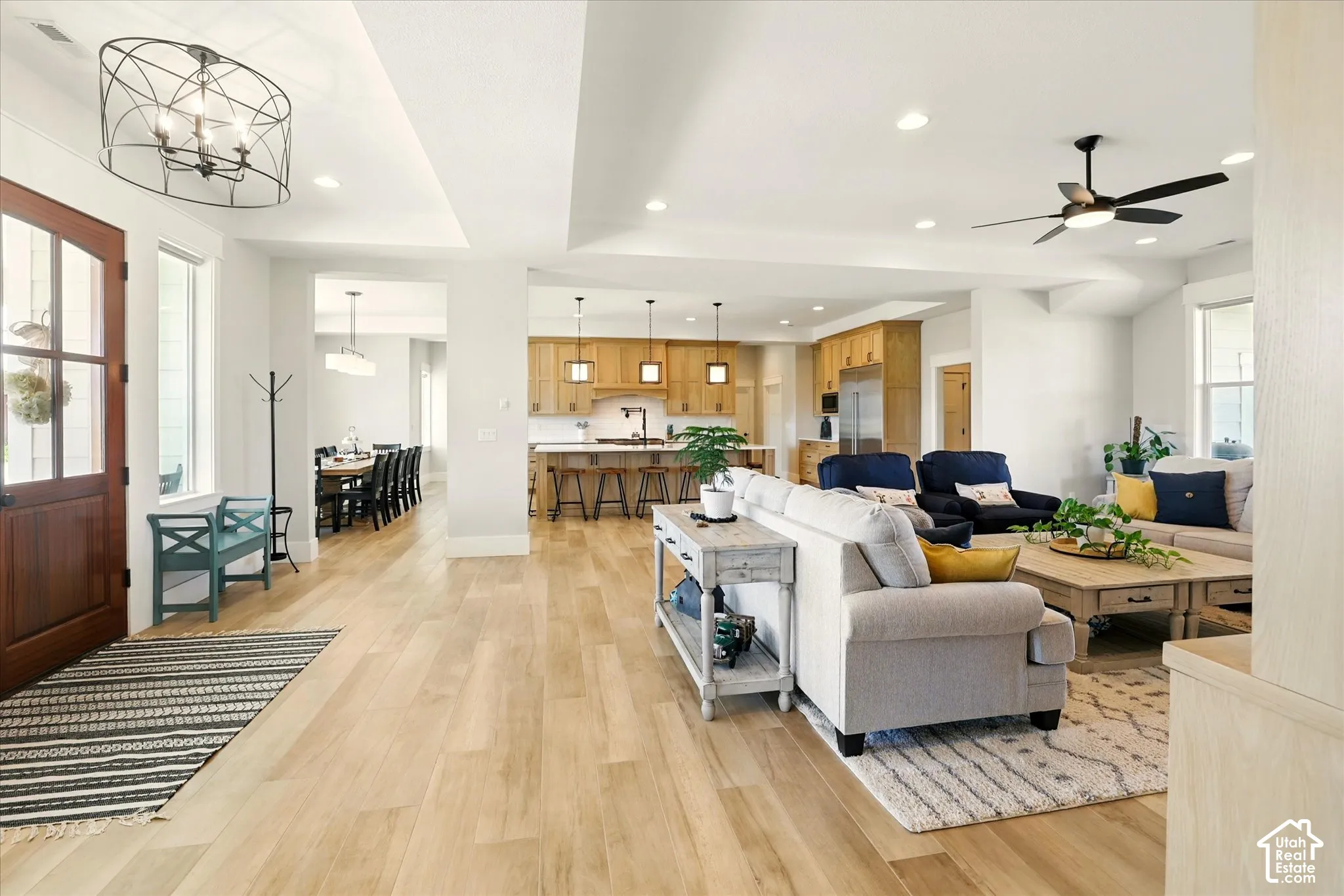 Open-concept interior featuring light wood-finish tile flooring, recessed lighting, a modern metal chandelier, and a kitchen with wood cabinetry and an island
