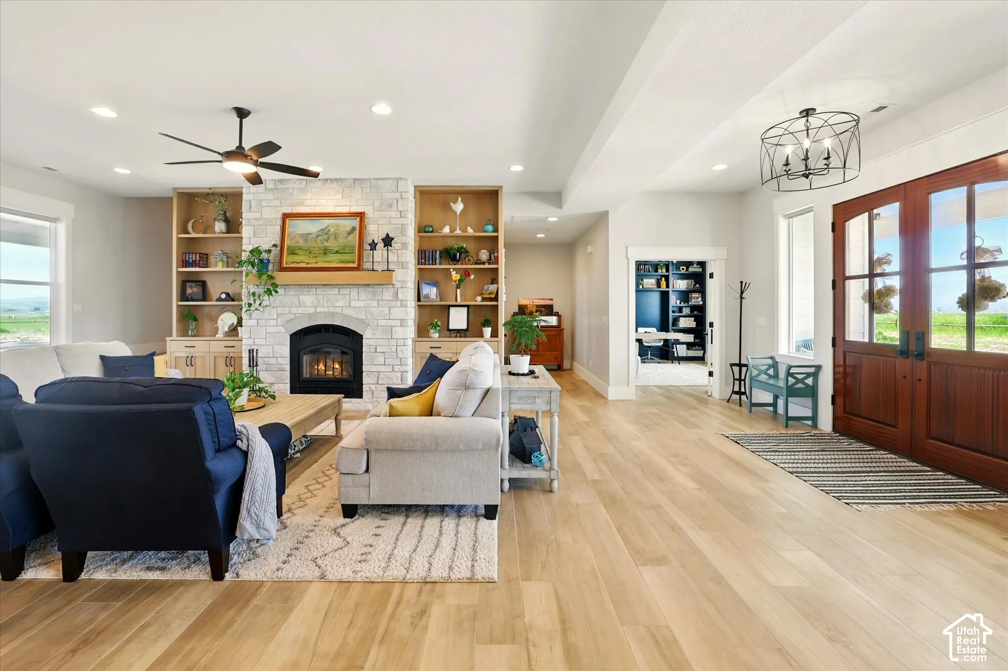 Living area featuring wood-finish tile flooring, stone-surround fireplace, floor-to-ceiling wood cabinetry, recessed lighting, and double-entry doors with glass inserts