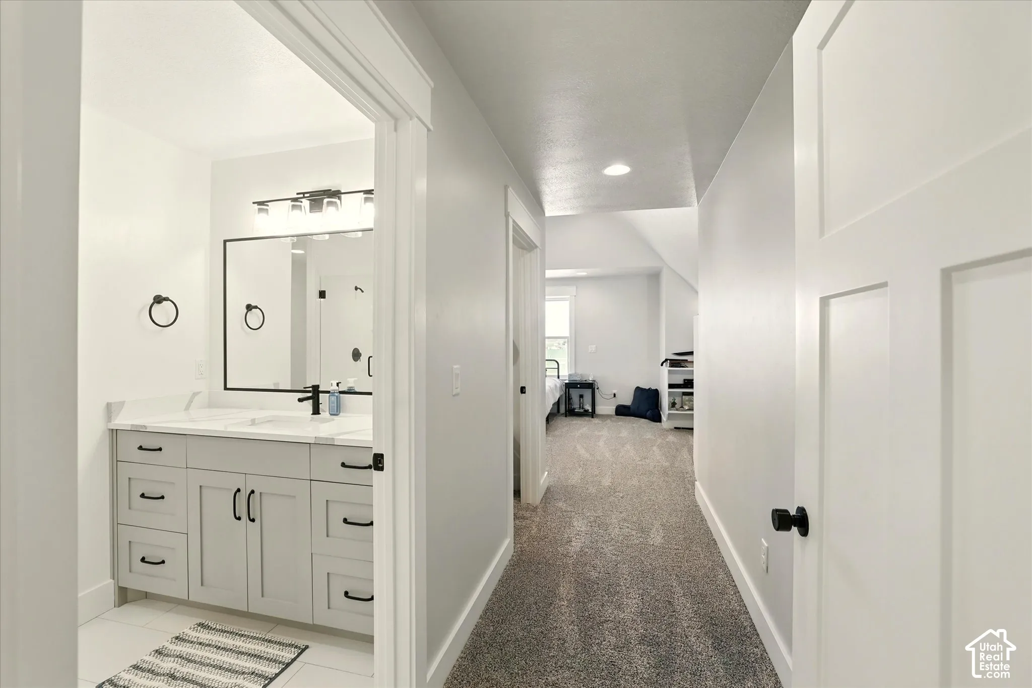 Entry into 2nd suite with hallway to bathroom, walk-in closet & bedroom. Bathroom vanity featuring light-toned cabinetry, undermount sink, and a stone-surface countertop, accented by a black-framed mirror and matching hardware