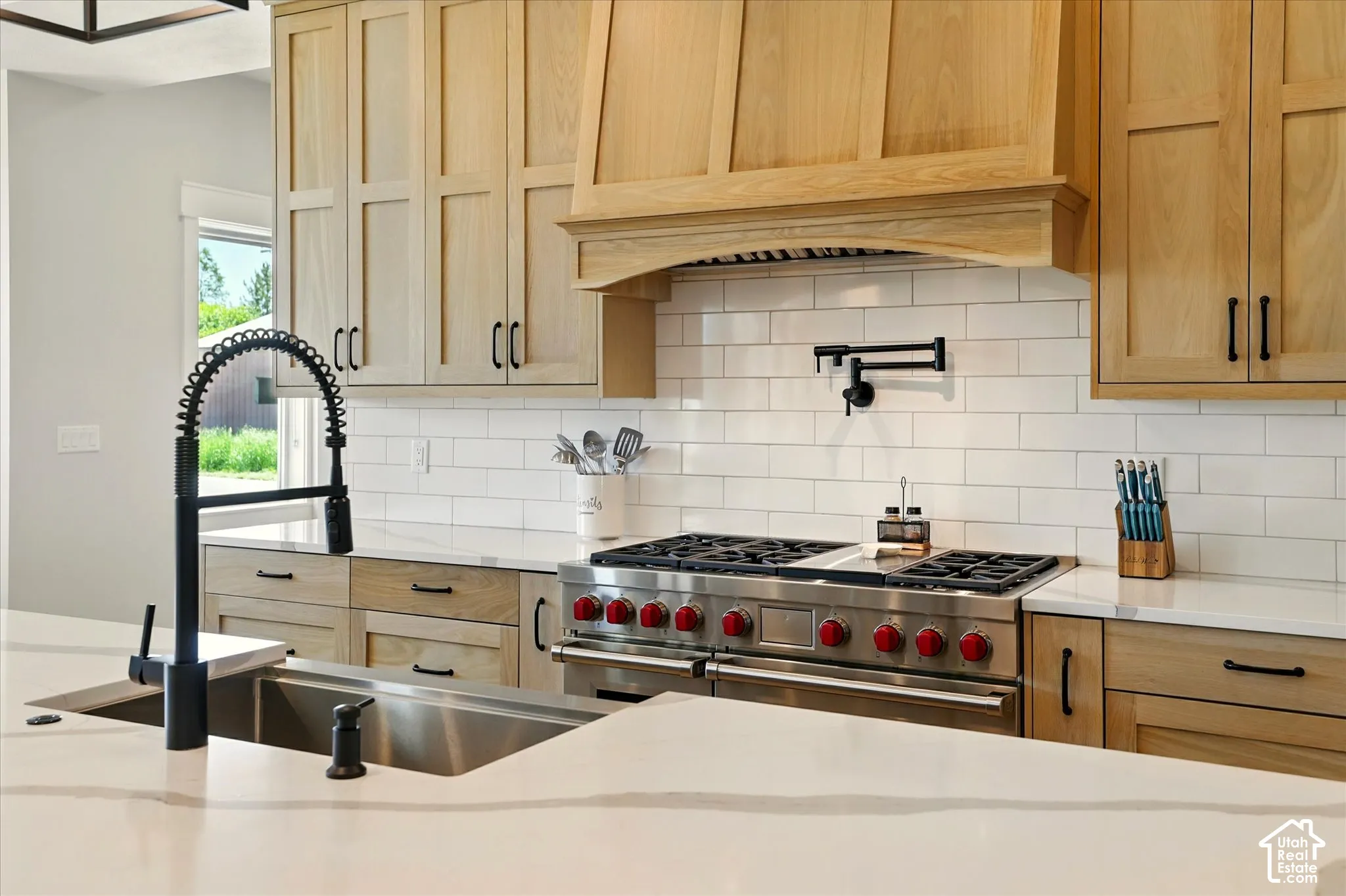Kitchen featuring light wood shaker-style cabinetry, white quartz countertops, a white subway tile backsplash, a professional-grade stainless steel range with a custom wood hood, and a matte black gooseneck faucet