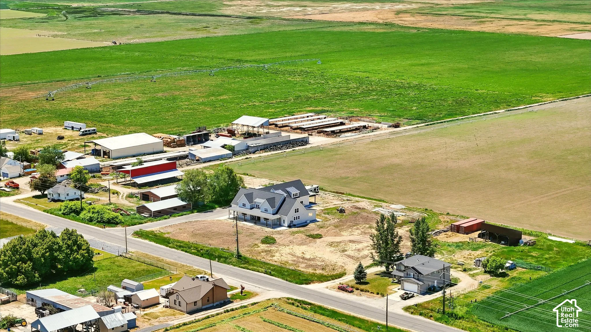 Aerial perspective of a sprawling rural acreage featuring extensive pasture land, multiple agricultural structures, and a residential dwelling with a covered porch