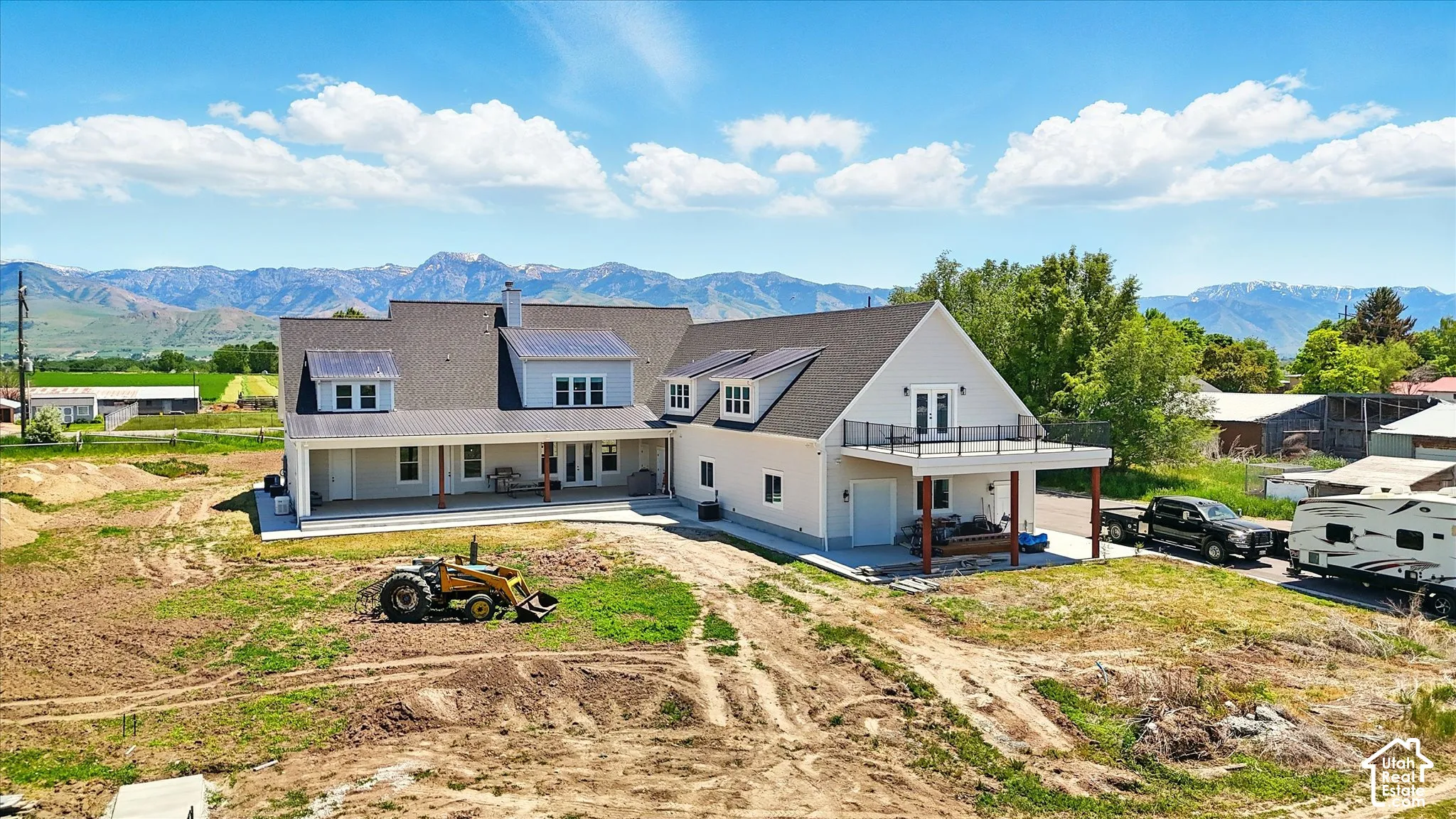 Two-story residence featuring light-toned siding, covered rear porch, upper-level balcony with metal railing, multiple dormer windows, and a mountain backdrop